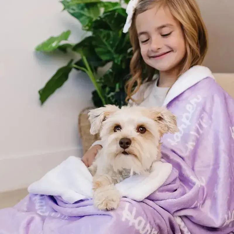 Une jeune fille souriante serrant un petit chien blanc dans un plaid personnalisé mauve avec du texte blanc