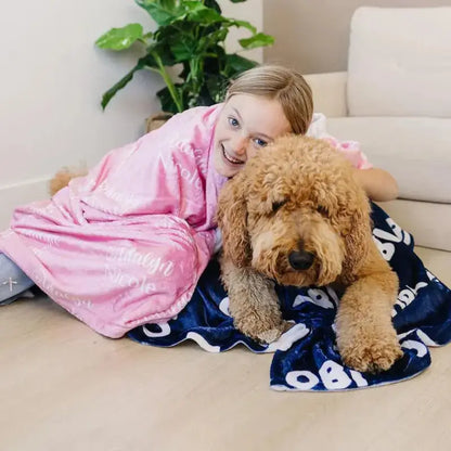 Une jeune fille riant en s'enroulant dans un plaid personnalisé rose avec un Doodle beige clair sur un plaid personnalisé bleu marine en dessous